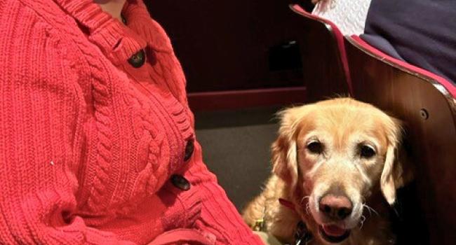 Sarah with Blue Hair and a red coat sitting with her guide dog knelt down in front of her