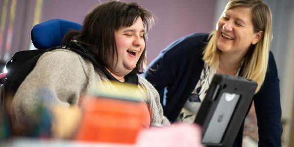 Carer and supporter laughing while looking at a tablet