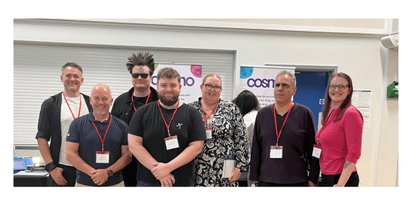 The AT team stood together smiling in front of conference boards