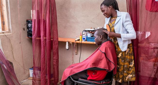 Man in a barber chair with Jane shaving his head in her salon