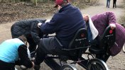 A man sitting in an adapted tricycle with three volunteers leaning over the bike