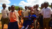 Avina Amos surrounded by his classmates, pushing his wheelchair