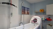 A white bath with controls on and an overhead shower with assistive hoists