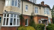 Exterior view of white bay windows and a sage coloured front door with bushes at the front of house