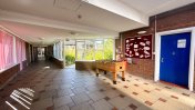 Red and cream tiled windowed corridor and foyer area with a fuseball table and a door leading outside to garden area