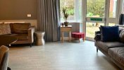 Lounge with oak laminate flooring with a brown sofa and a windowed fire door that opens out into garden area