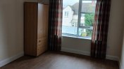A dark oak laminated floor with an oak wardrobe in the top left hand corner next to double glazed white windows and brown checked floor length curtains
