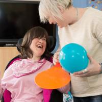 Staff member holding a table tennis bat and balloon next to a resident laughing 
