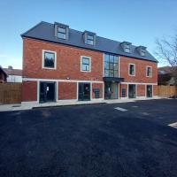 A red bricked new build block of flats with a black tarmacked car park in front of it