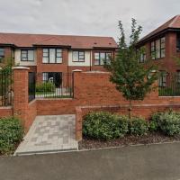 A complex of red bricked two storey buildings surrounded by black gated walls and shrubbery with disabled car parking spaces in front of it