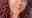 A portrait shot of Tina with reddish brown curly long hair smiling at the camera wearing a grey top 