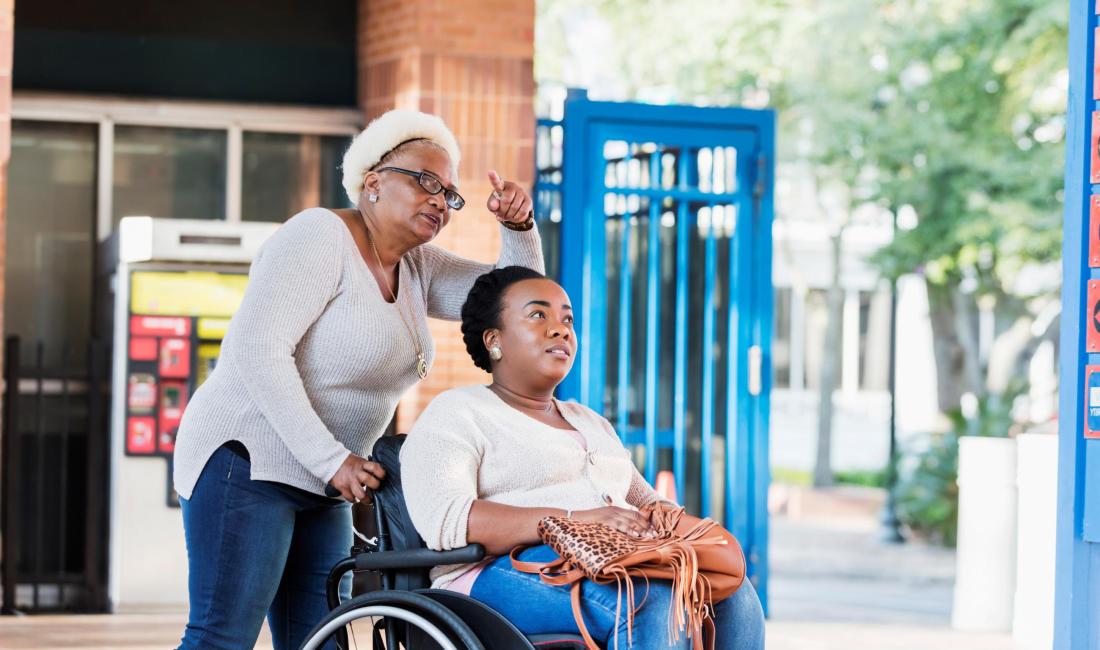 A woman in a wheelchair, being pushed by an older woman who is pointing at something